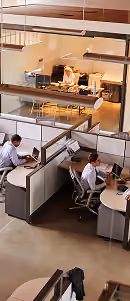Office workspace with multiple employees working at desks separated by cubicle walls.