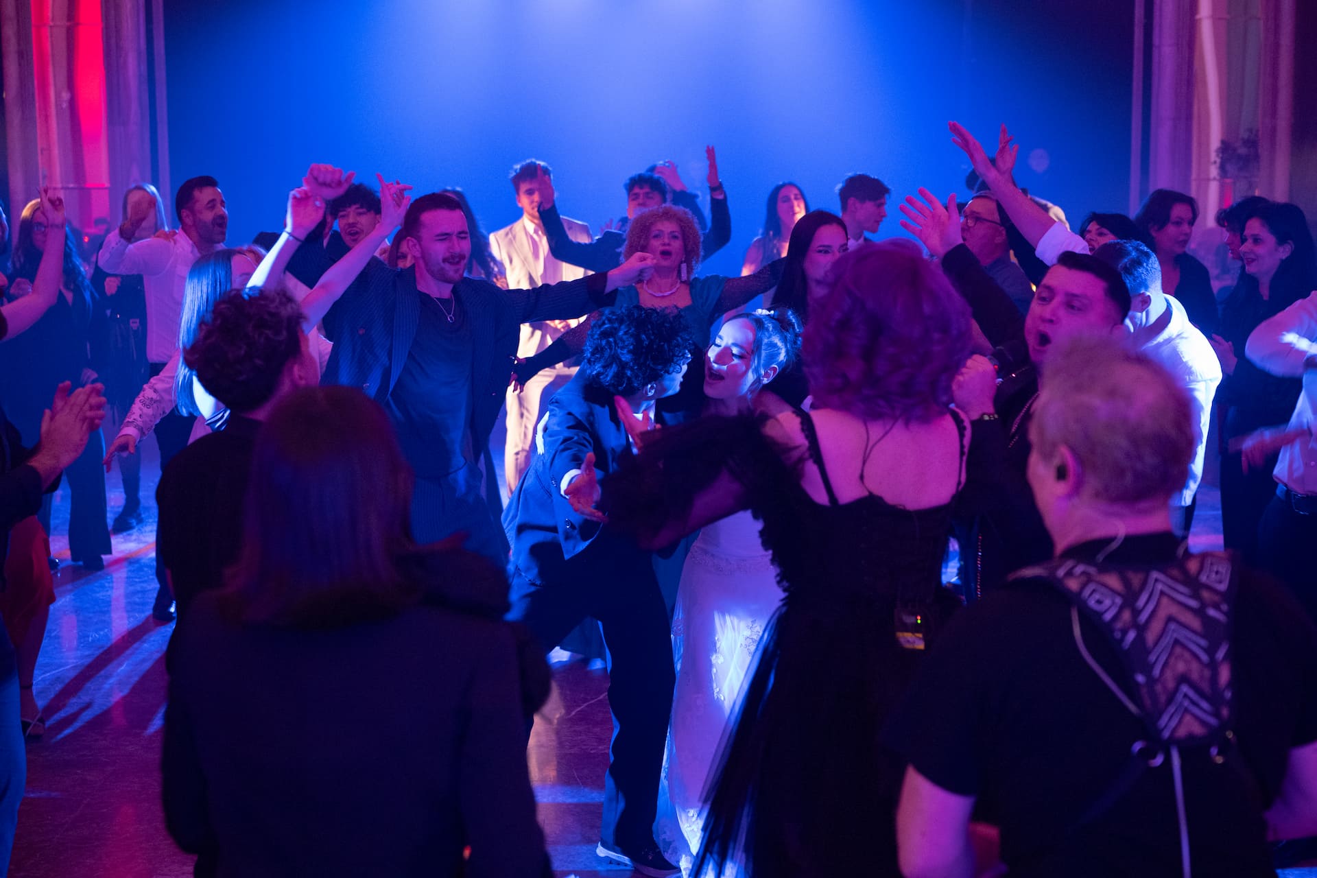 Un grup mare de oameni dansează și se bucură într-un club de noapte cu iluminare albastră și violetă.