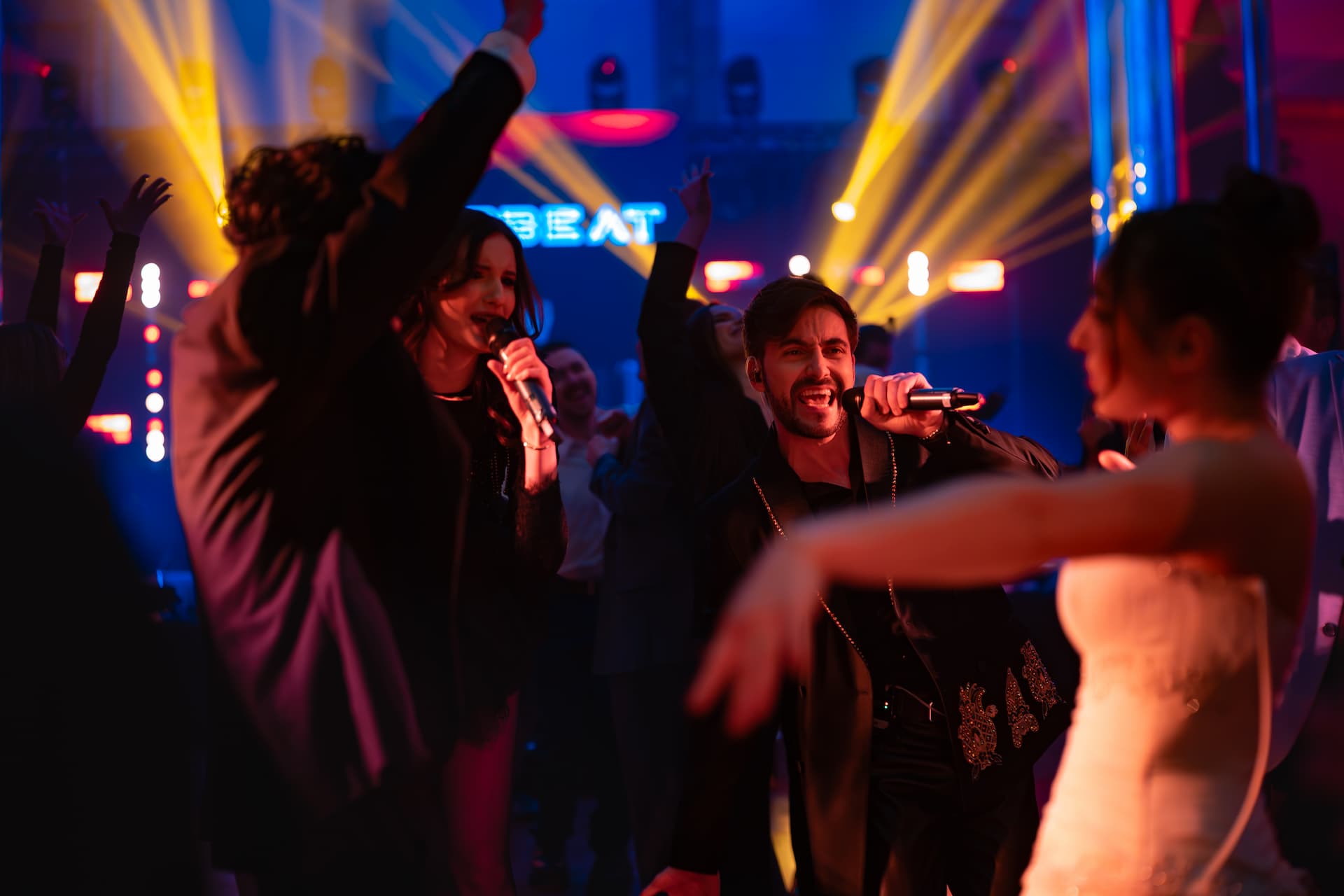 Oameni cântând și dansând la un concert vibrant cu lumini colorate în fundal.