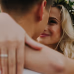 Cuplu îmbrățișându-se strâns, femeie zâmbitoare cu păr blond și coroniță de flori.