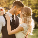 Cuplu îmbrăcat elegant, îmbrățișându-se în aer liber într-o zi însorită.