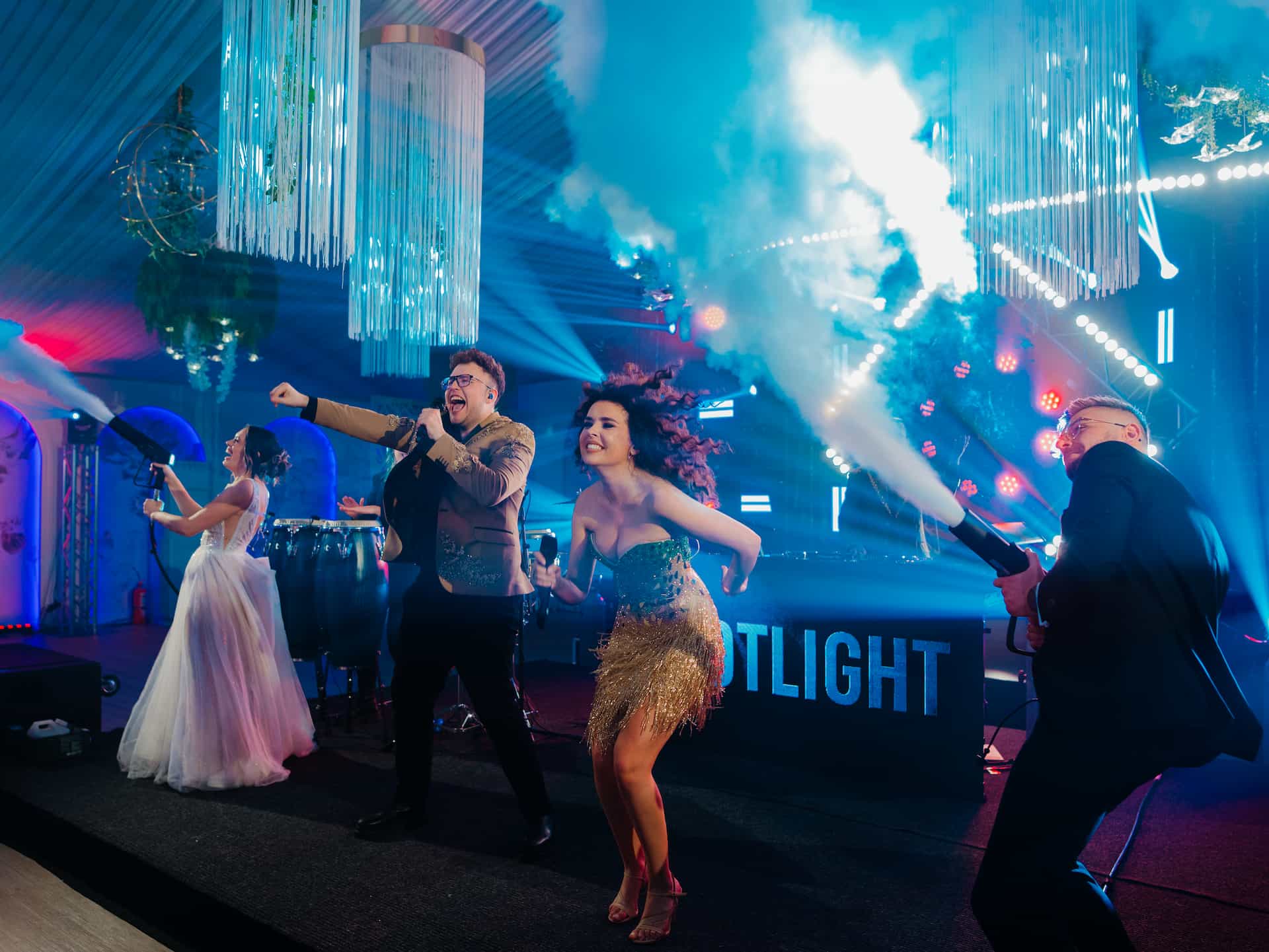 Tineri cântă și dansează pe o scenă cu lumini colorate și fum emis din tunuri speciale.