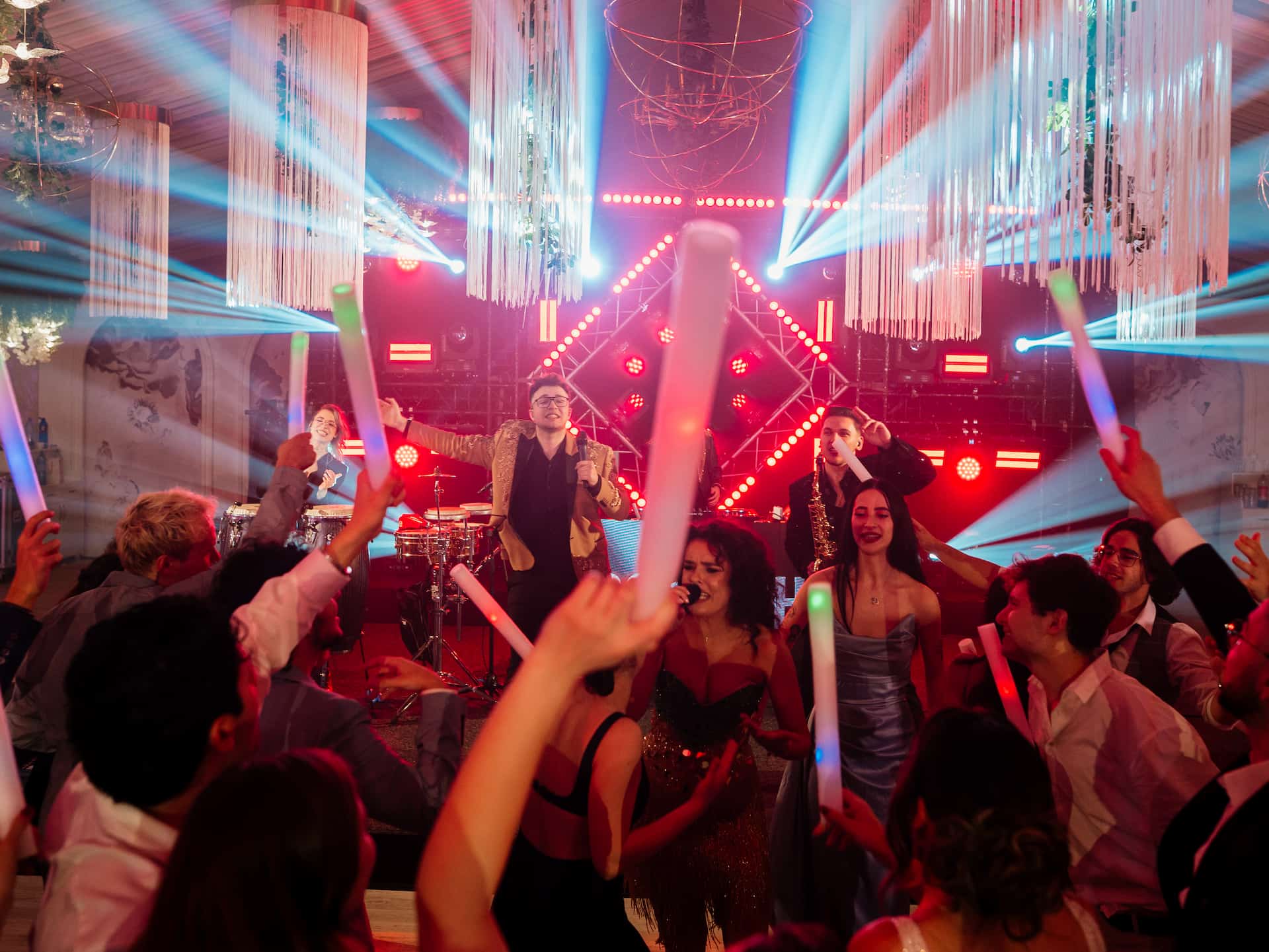 O gașcă de oameni petrecând și dansând la un concert cu lumini strălucitoare și bețe luminoase în mână.