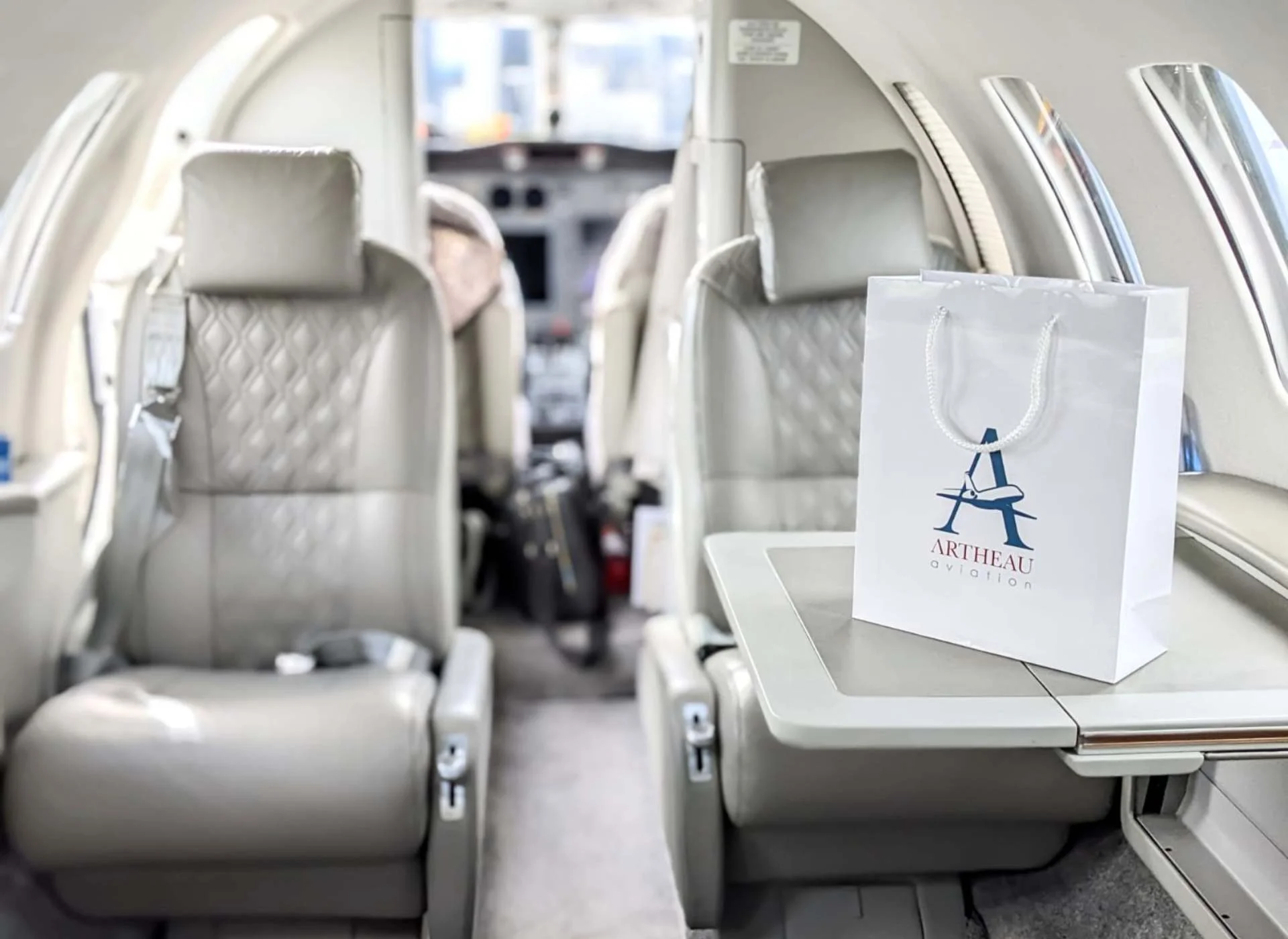 Interior of a Cessna Citation II private jet with leather seats and an Artheau Aviation gift bag placed on the fold-out table.