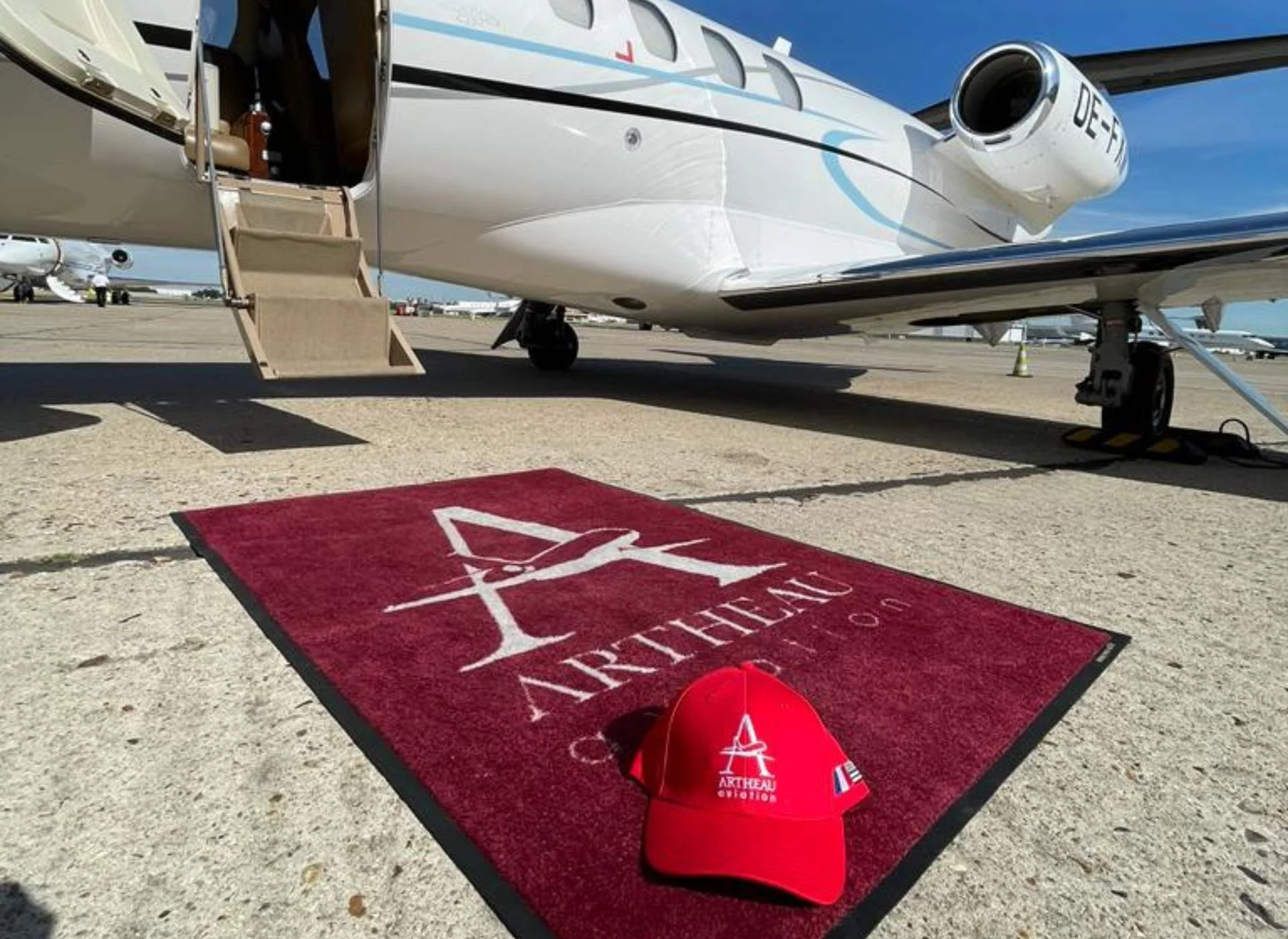 Jet privé Cessna Citation II sur le tarmac avec porte ouverte, tapis d’accueil Artheau Aviation et casquette rouge brandée au premier plan.