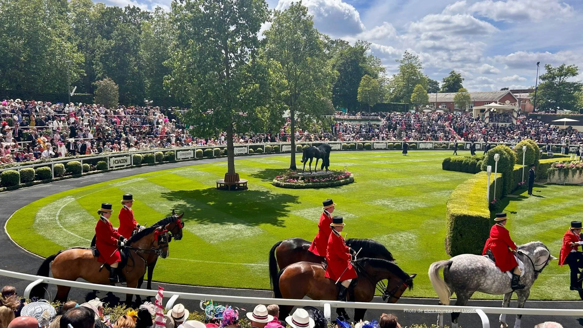Royal procession at Royal Ascot with riders in red livery in front of packed grandstand