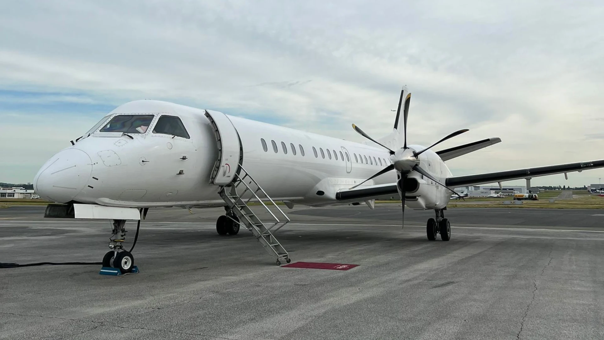 Front three-quarter view of a Saab 2000 aircraft parked on the apron with boarding stairs