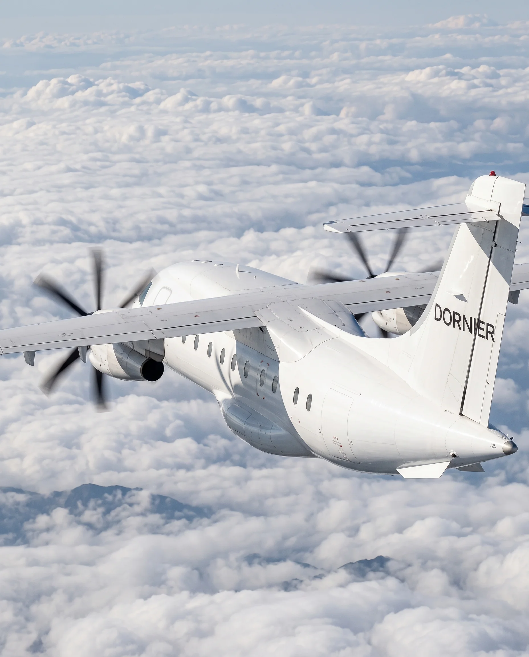 Rear view of a Dornier 328 aircraft banking above clouds, showing the tail fin