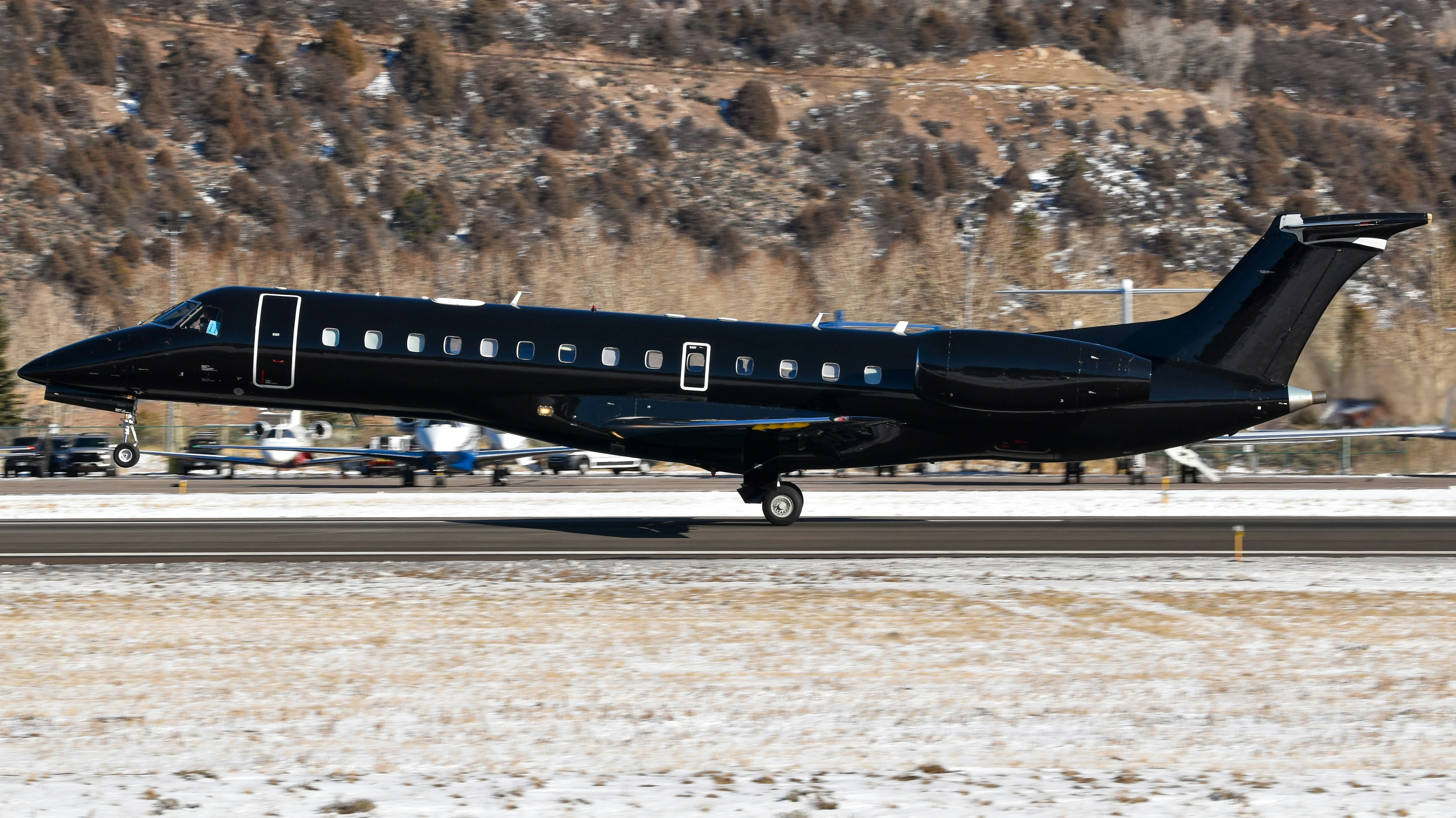 ERJ145 aircraft in black livery landing with snow-covered mountains in the background