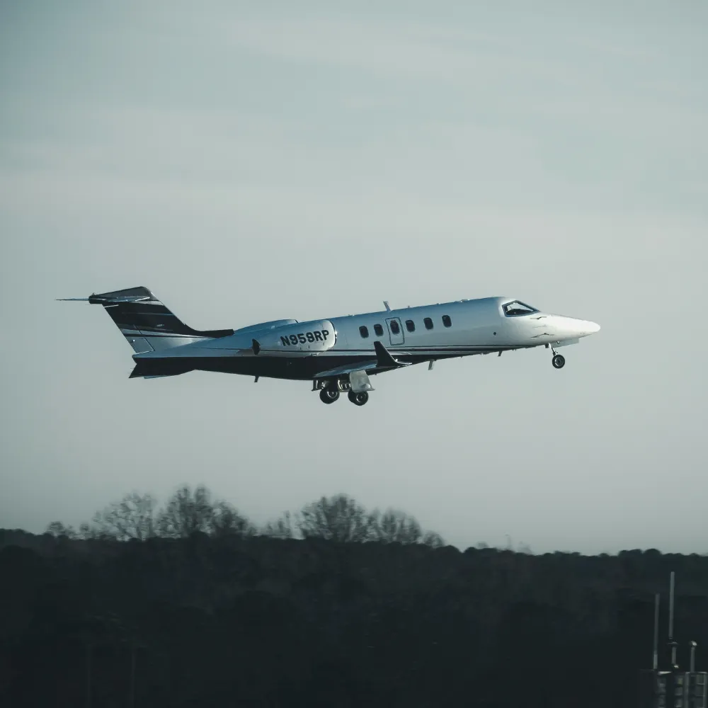 Jet privé en phase de décollage, train d'atterrissage sorti, sur fond de ciel gris et de forêt