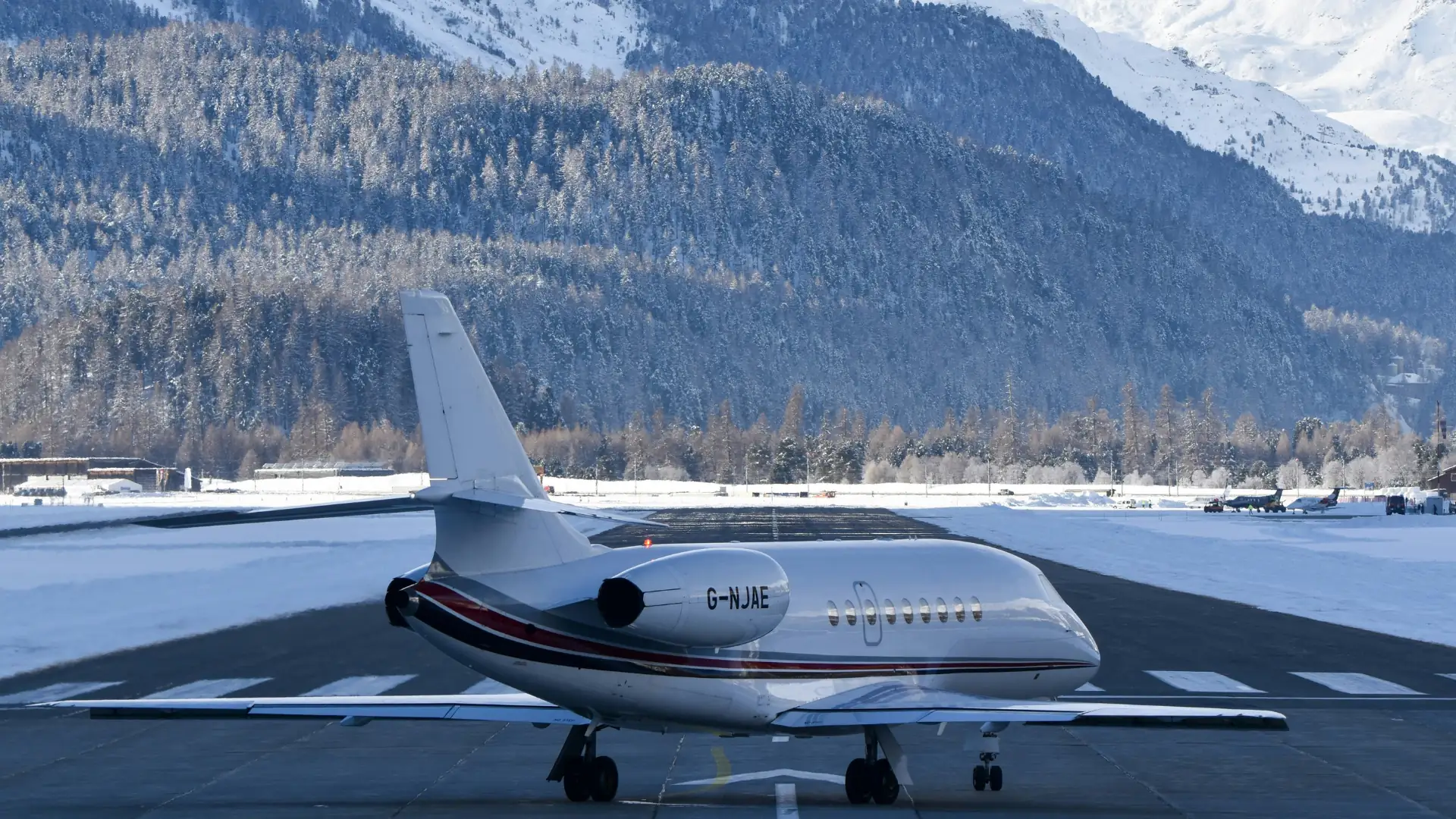 Jet privé sur la piste d'un aéroport de montagne enneigé, entouré de forêts et de sommets alpins