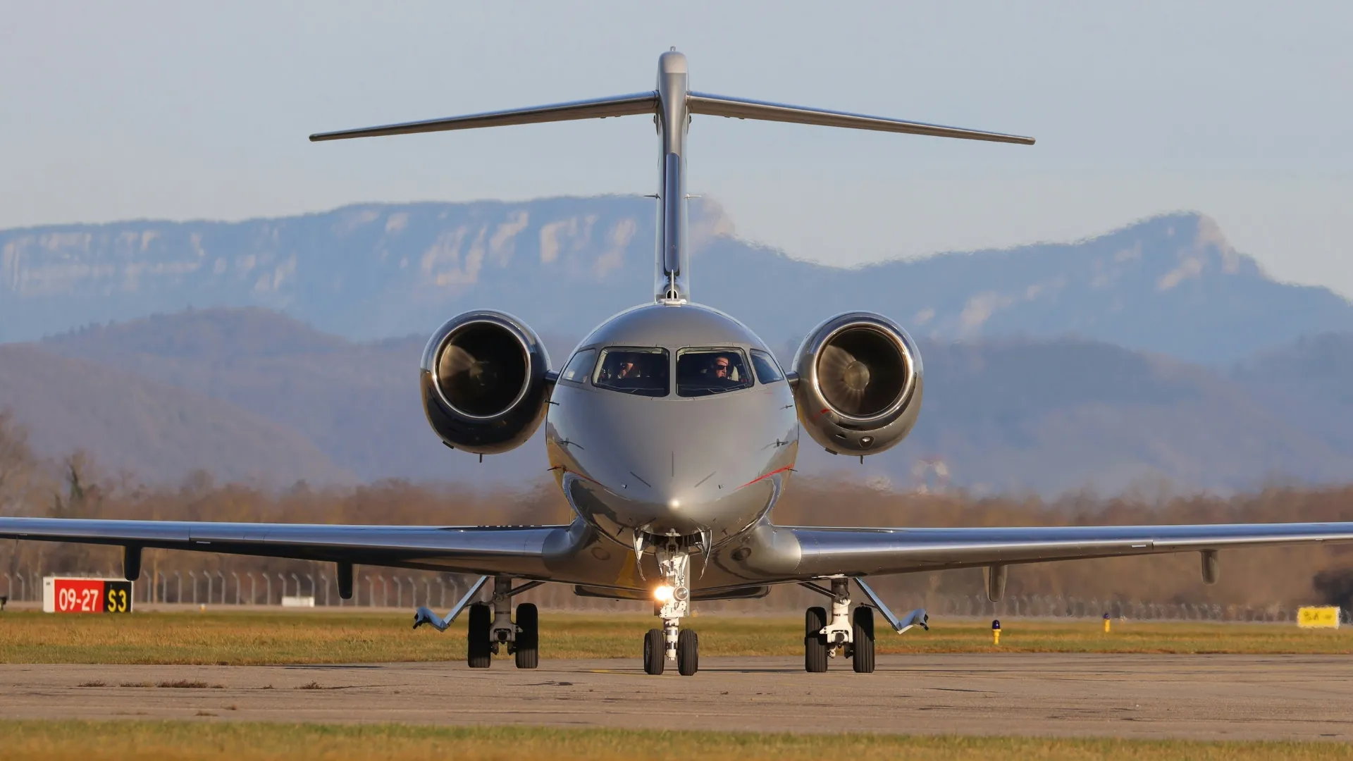 Jet d'affaires en roulage vers la piste, vu de face avec les pilotes dans le cockpit et des montagnes en arrière-plan