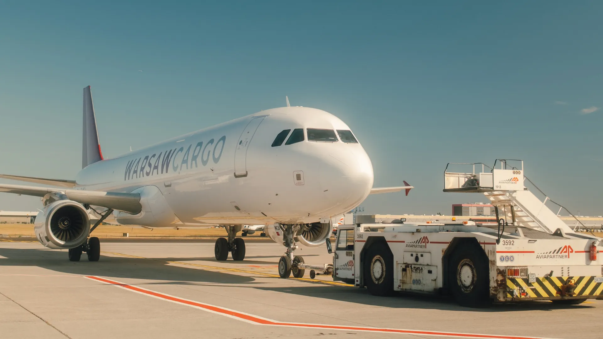 Avion cargo remorqué par un tracteur de piste sur le tarmac d'un aéroport, sous un ciel bleu dégagé