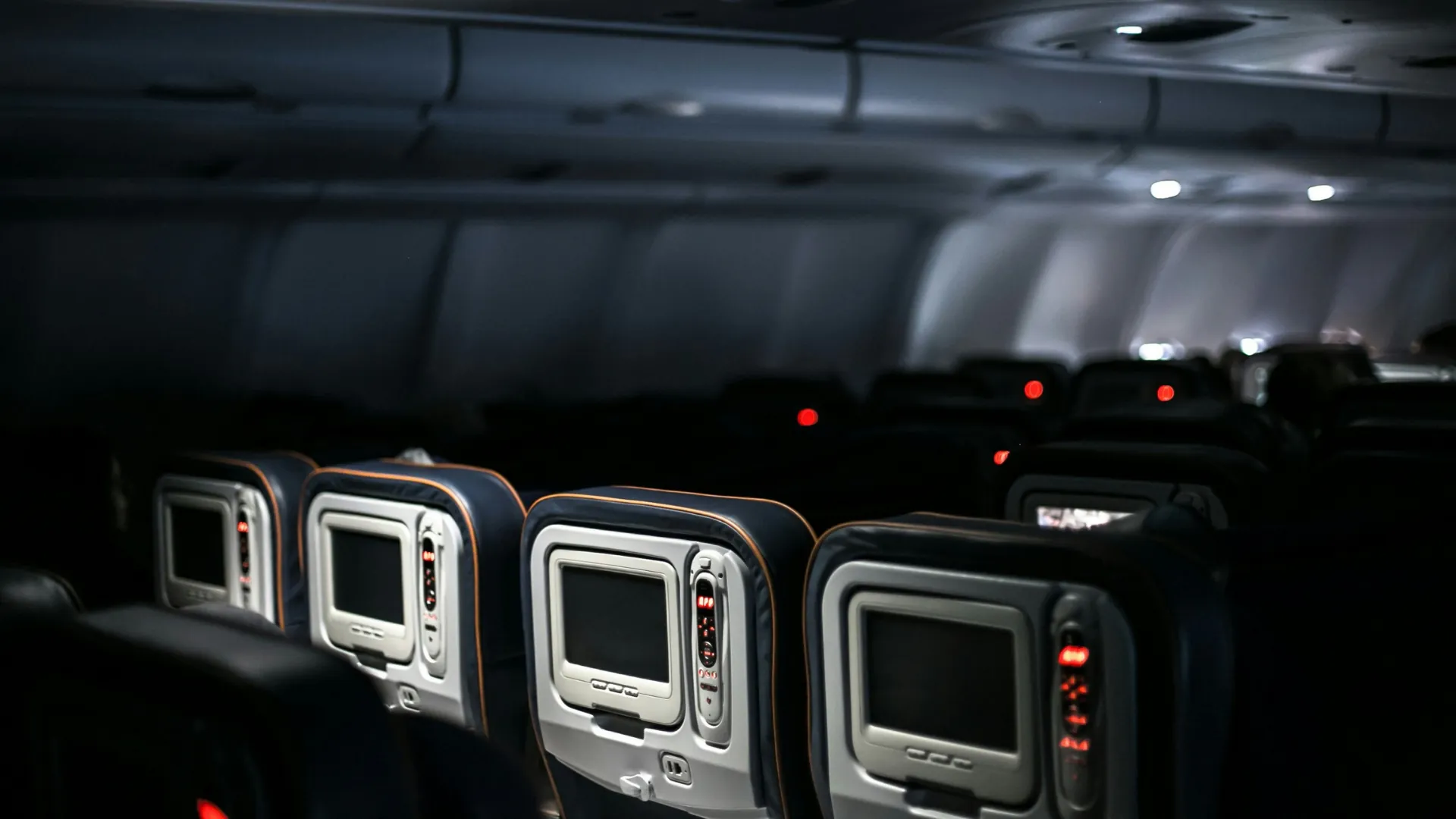 Cabine d'avion plongée dans la pénombre pendant un vol de nuit, avec des écrans de divertissement au dos des sièges