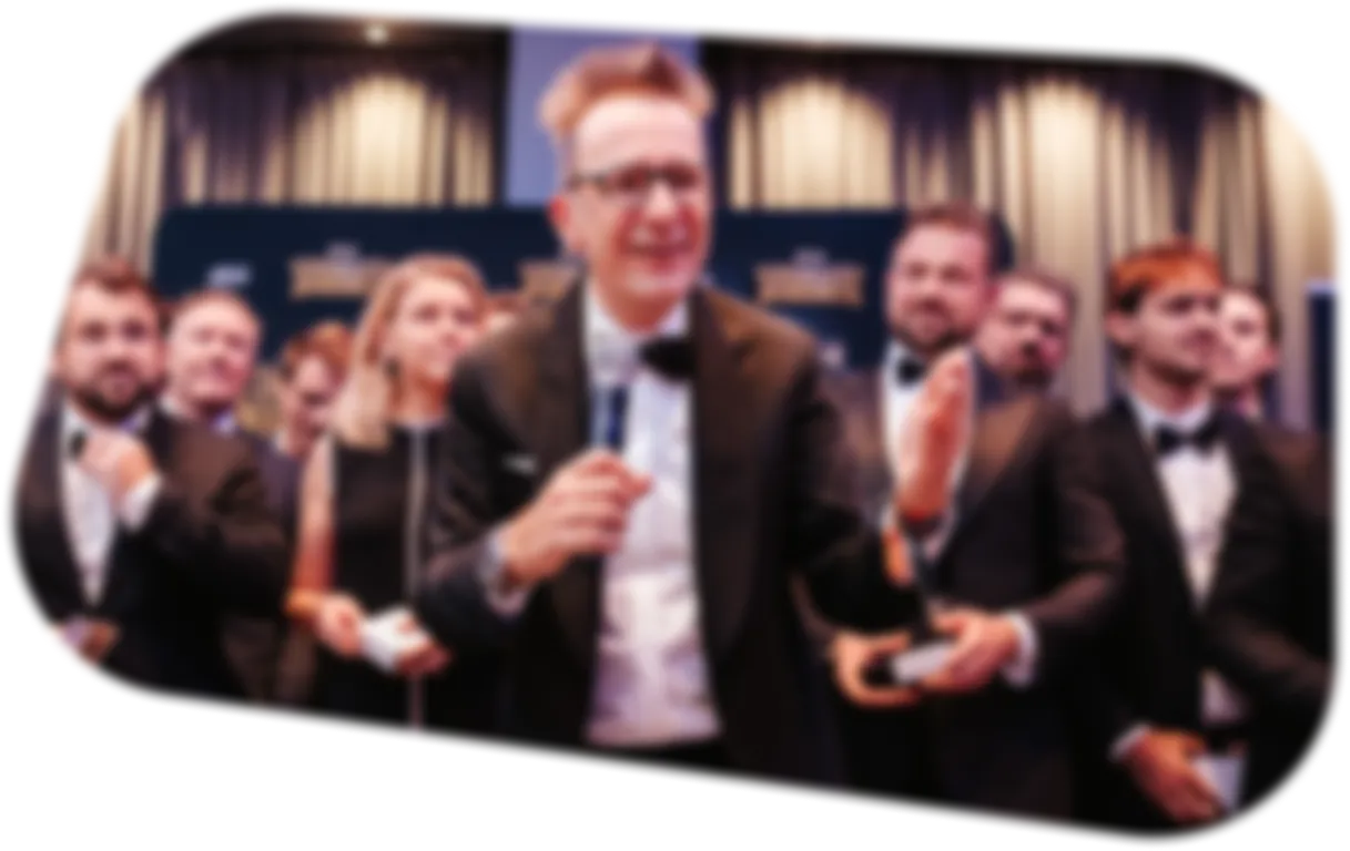 Gruppe von Menschen in formeller Kleidung bei einer Preisverleihung, ein Mann spricht ins Mikrofon.