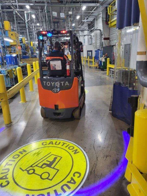 Chariot élévateur Toyota orange dans un entrepôt industriel avec panneau de prudence