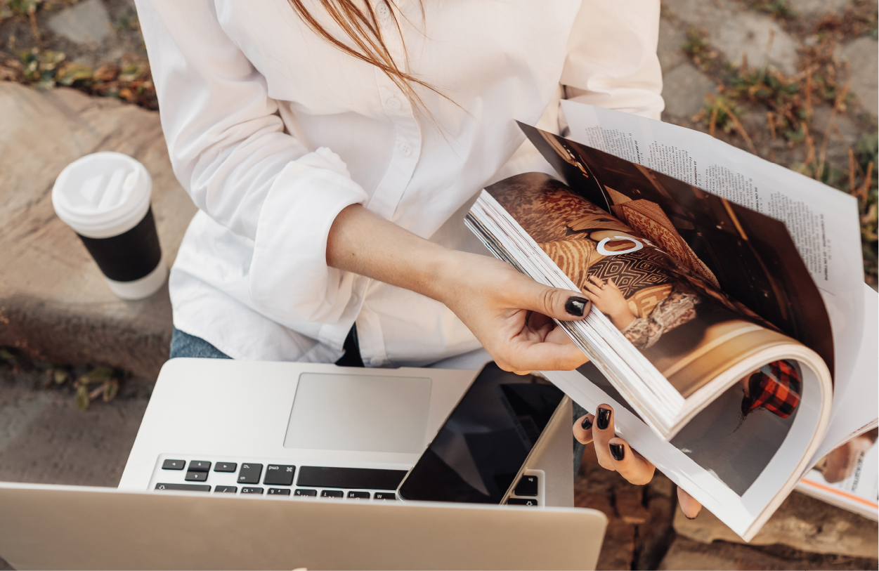 Accelerated Impact Title: shows a woman holding open a magazine while browsing on digital devices.