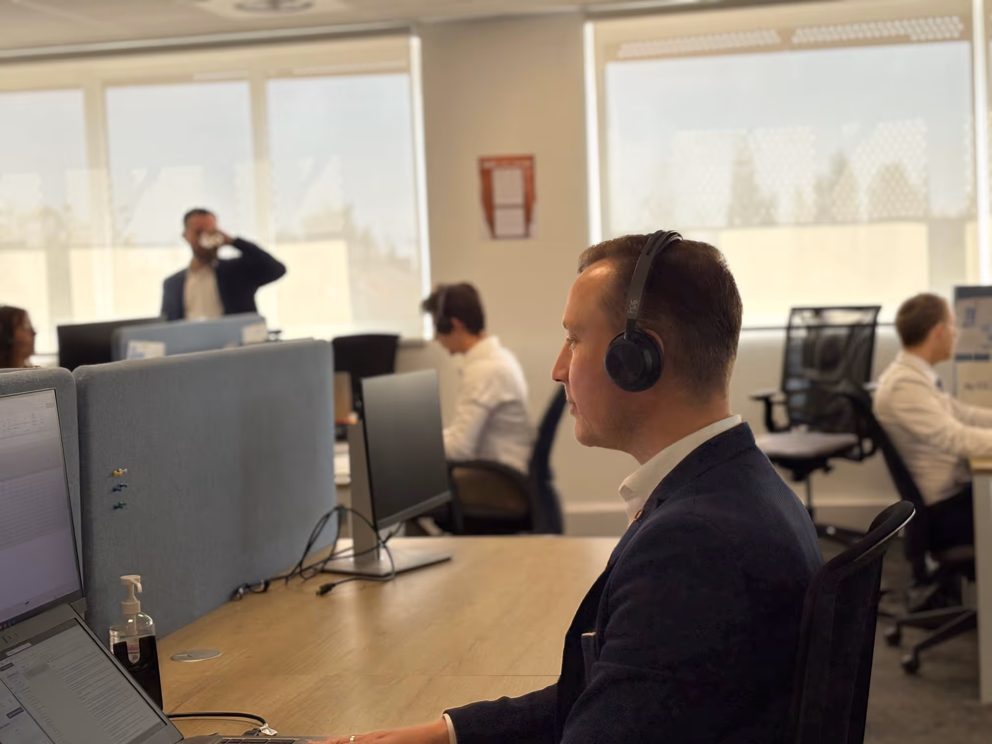 Expert DUNE Energie portant un casque au bureau travaillant devant un ordinateur portable avec d'autres collègues autour.