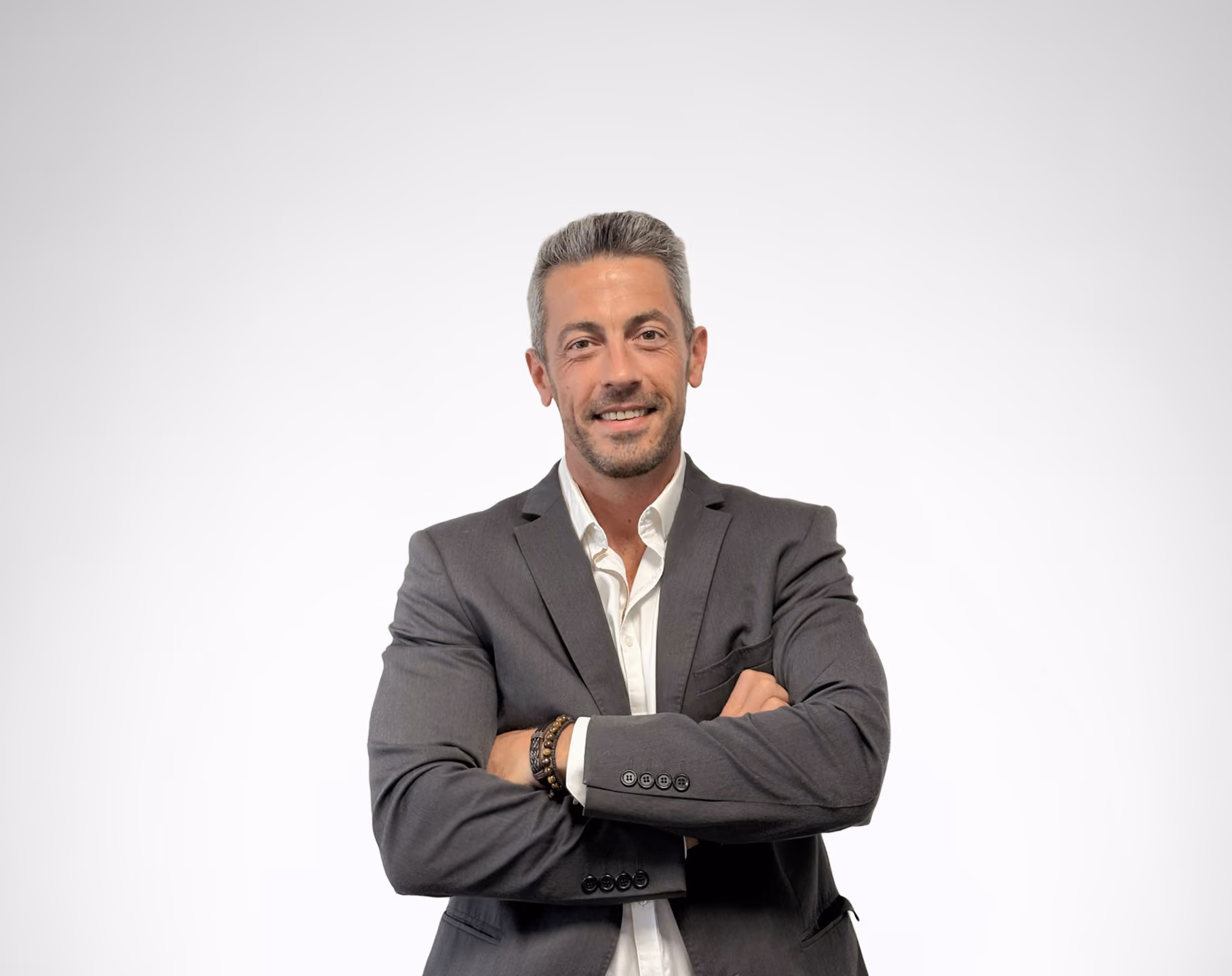 Homme souriant bras croisés en costume gris avec chemise blanche sur fond clair.