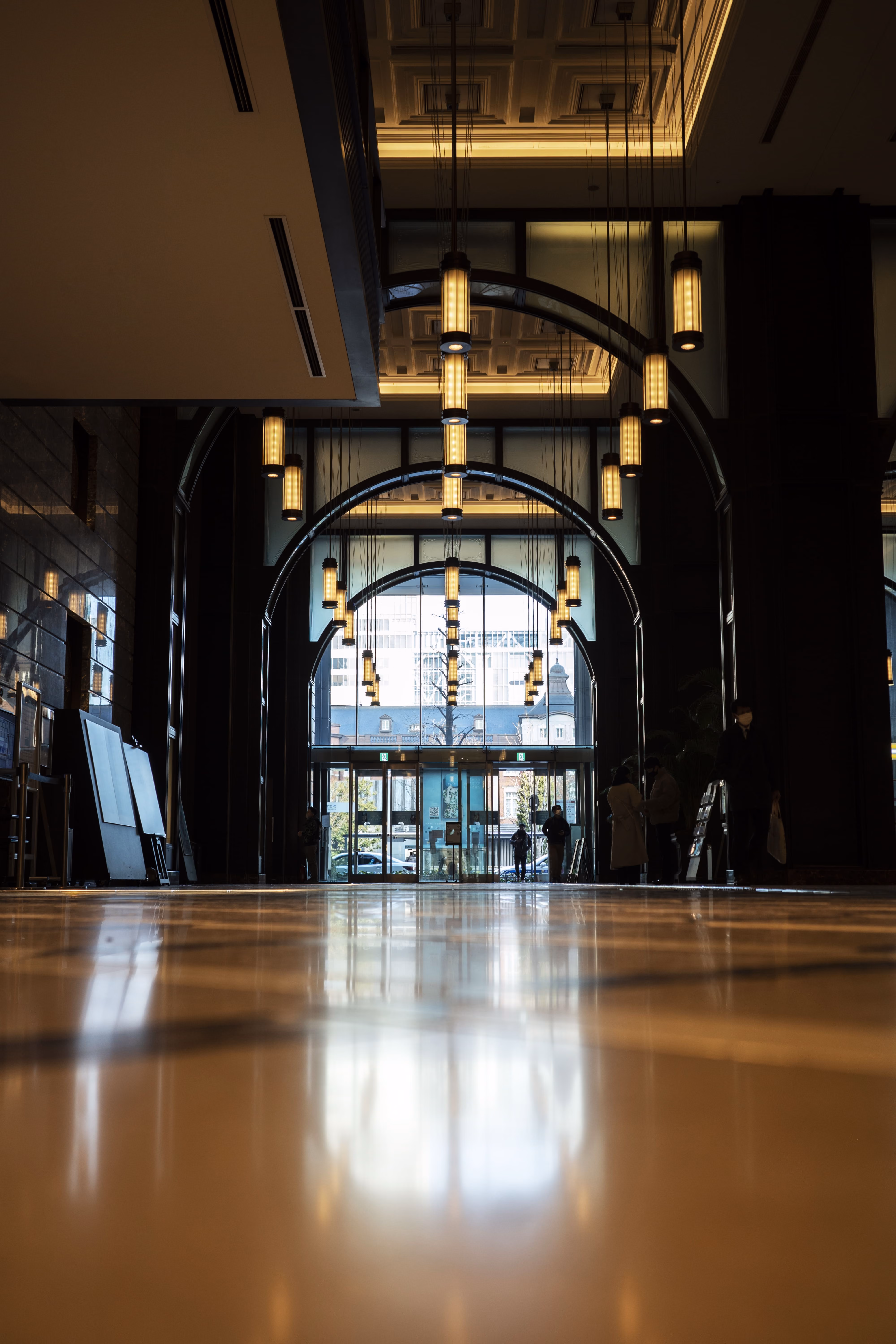 Intérieur d'un hall d'entrée d'hôtel avec suspensions lumineuses et silhouettes de personnes.