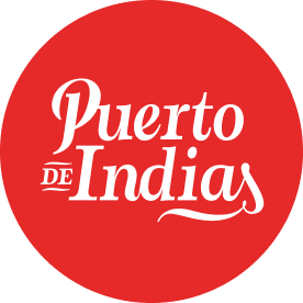 Logotipo circular rojo con el texto "Puerto de Indias" en blanco, con un estilo tipográfico elegante.
