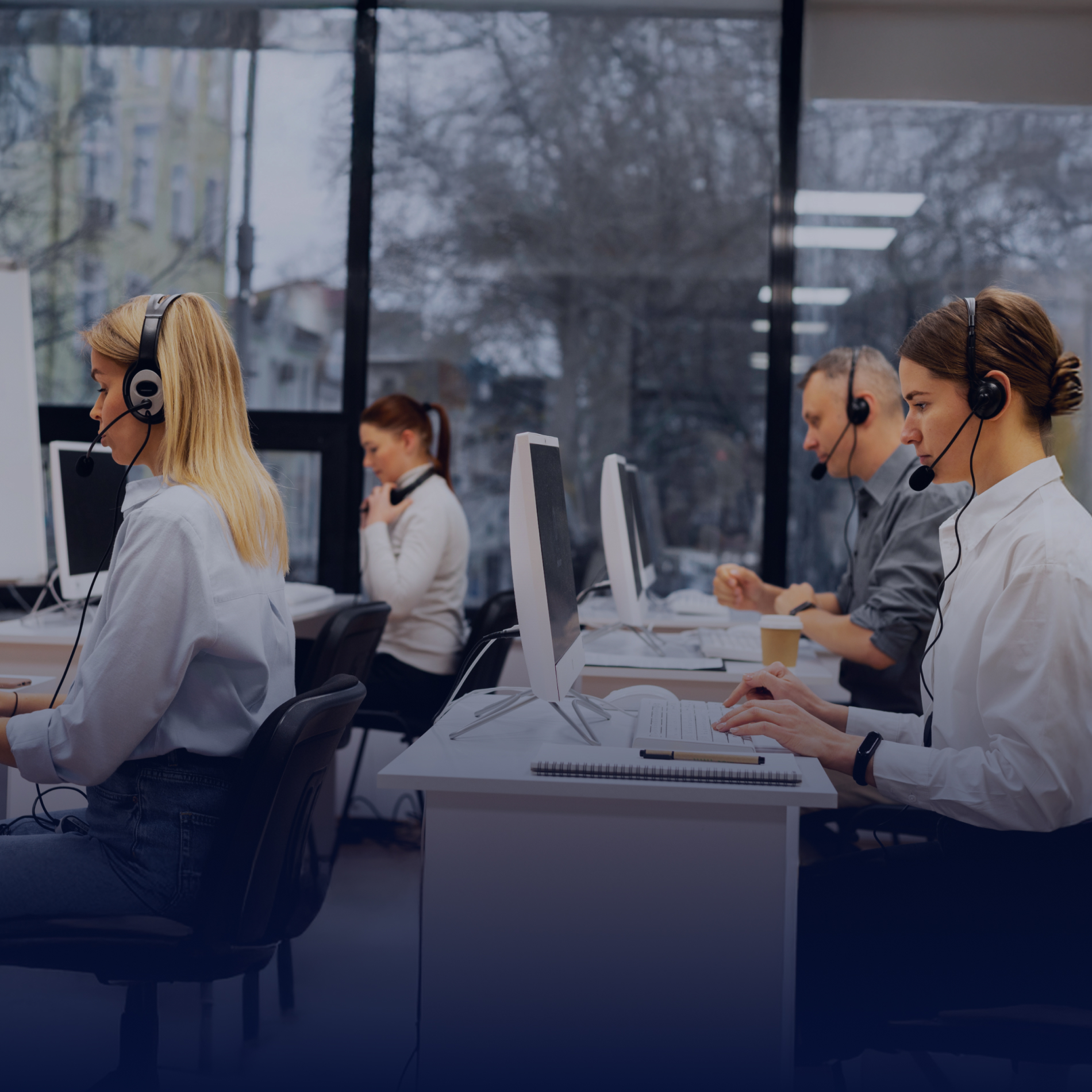 Cuatro personas en un call center, usando auriculares y trabajando en computadoras en un ambiente moderno y luminoso.