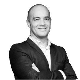 Hombre con cabello corto y sonrisa, vestido con chaqueta negra y camisa blanca, brazos cruzados sobre el pecho.