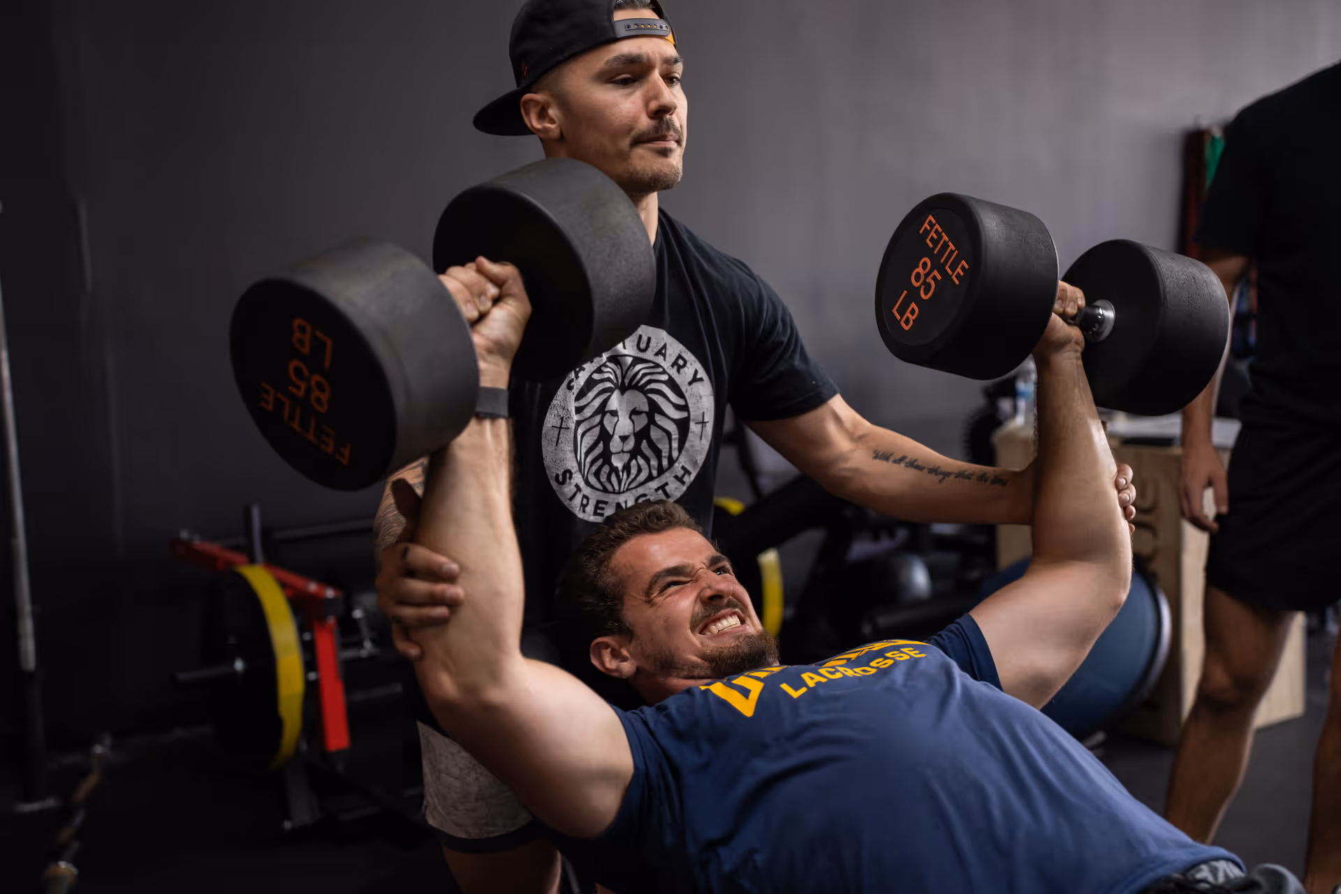 An older man lifting dumbbells supported by a personal trainer at Sanctuary Strength in Franklin, TN