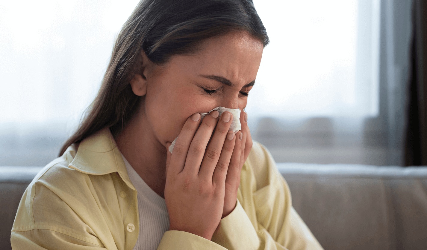 Woman sneezing into a tissue due to severe allergy symptoms at home, representing chronic sinus issues and care from the best allergy doctor in Los Angeles.