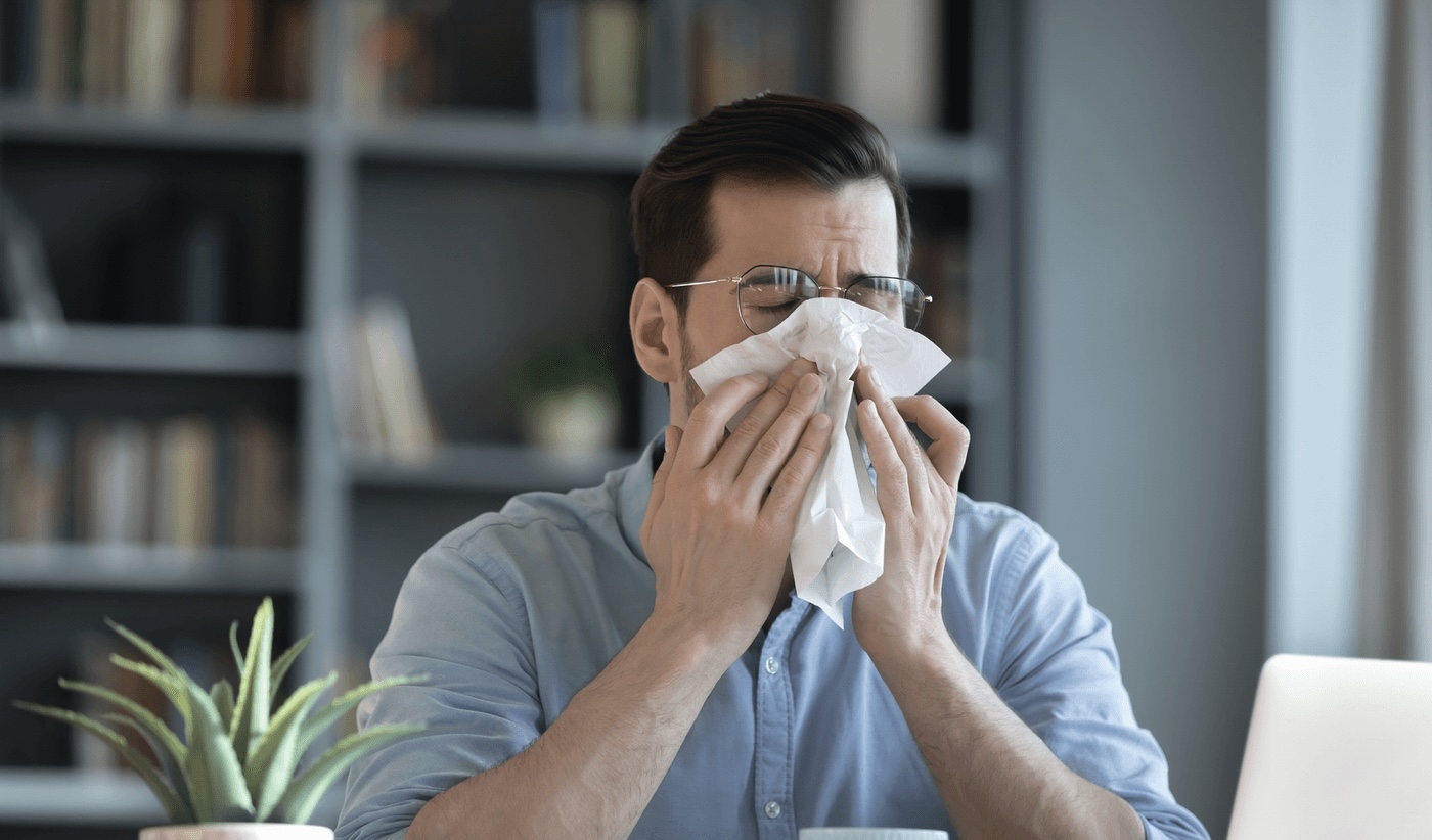 Man sneezing into a tissue while working at home, showing allergy symptoms that need to be treated by the best allergy doctor in Los Angeles, CA.