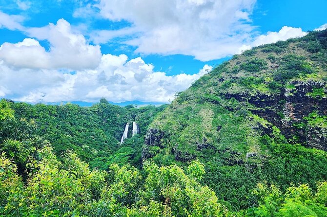 Waterfalls falling down a green ridge under a blue sky on Kauai