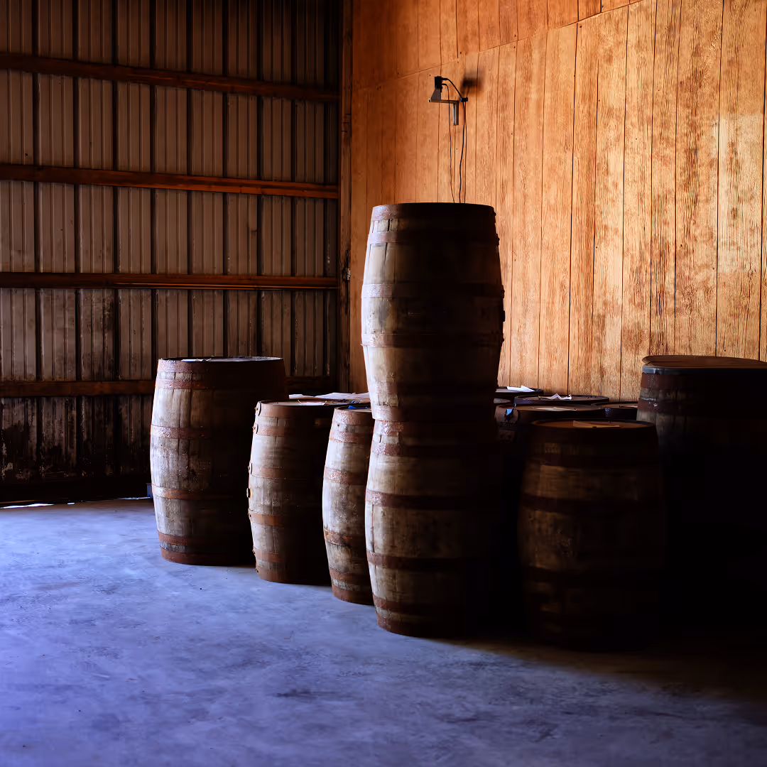 Oak whiskey barrels aging against the wooden wall of a Kentucky rickhouse.