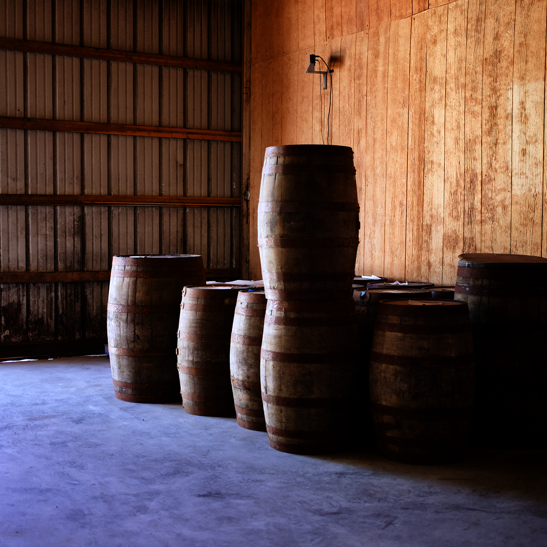 Oak whiskey barrels aging against the wooden wall of a Kentucky rickhouse.