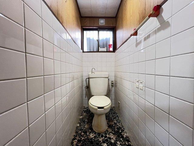 Narrow toilet room with white tiled walls and terrazzo-style flooring