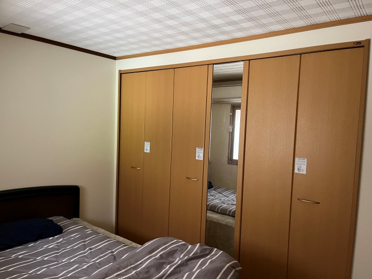 A bedroom with modern built-in closets featuring light wood doors, a double bed with striped bedding, and a textured ceiling.