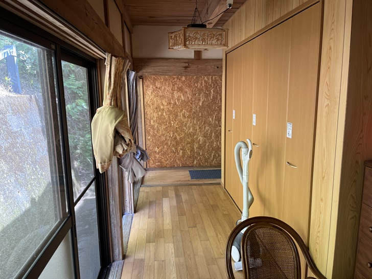 A hallway with wooden flooring, traditional wooden beam ceiling, and light wood closet doors. A decorative wooden carving or sign is visible on the wall.