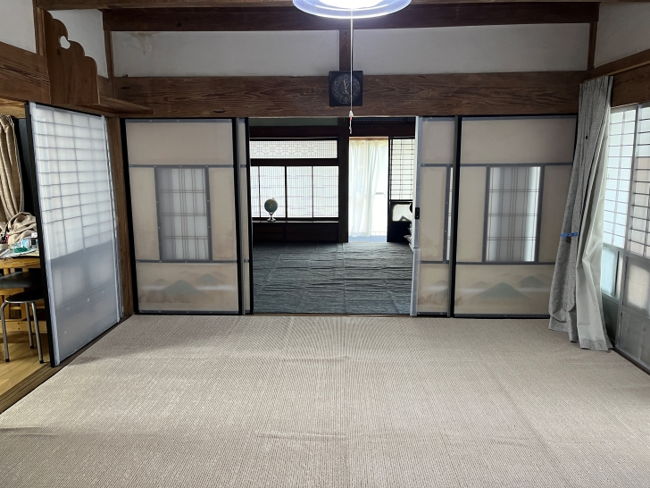 A traditional Japanese room with sliding shoji screens, exposed wooden beams, and tatami mat flooring. The screens create a serene, minimalist space with natural light filtering through.