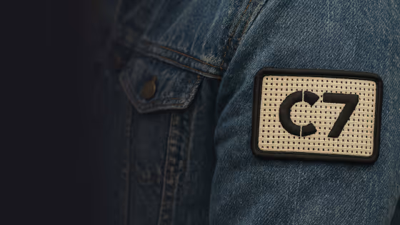 Close-up of a denim jacket sleeve with a beige patch labeled C7 sewn on it.