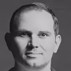 Black and white headshot of a man with short hair and a neutral expression on a gray background.
