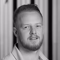 Black and white portrait of a man with short hair and beard, smiling slightly, against a blurred background.