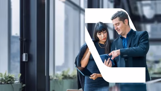 Two business professionals in dark attire looking at a smartphone in a modern glass office.