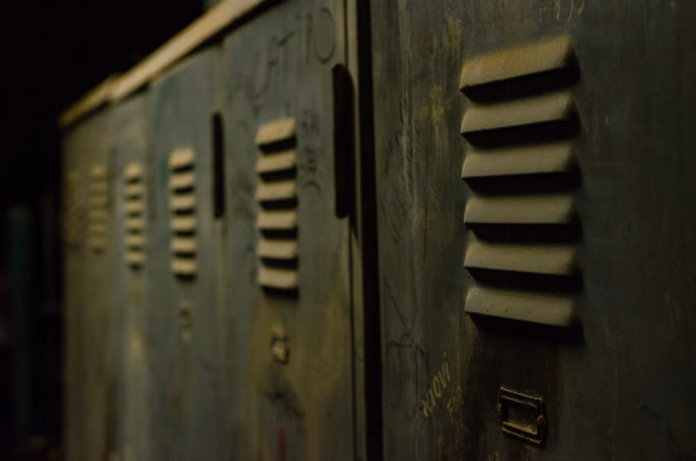 Close-up of old, worn metal lockers with ventilation slits in dim lighting.