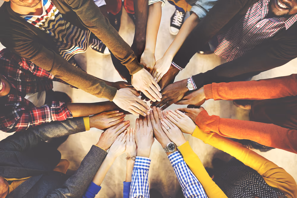 Diverse group of people placing hands together in a circle, symbolizing teamwork and unity.