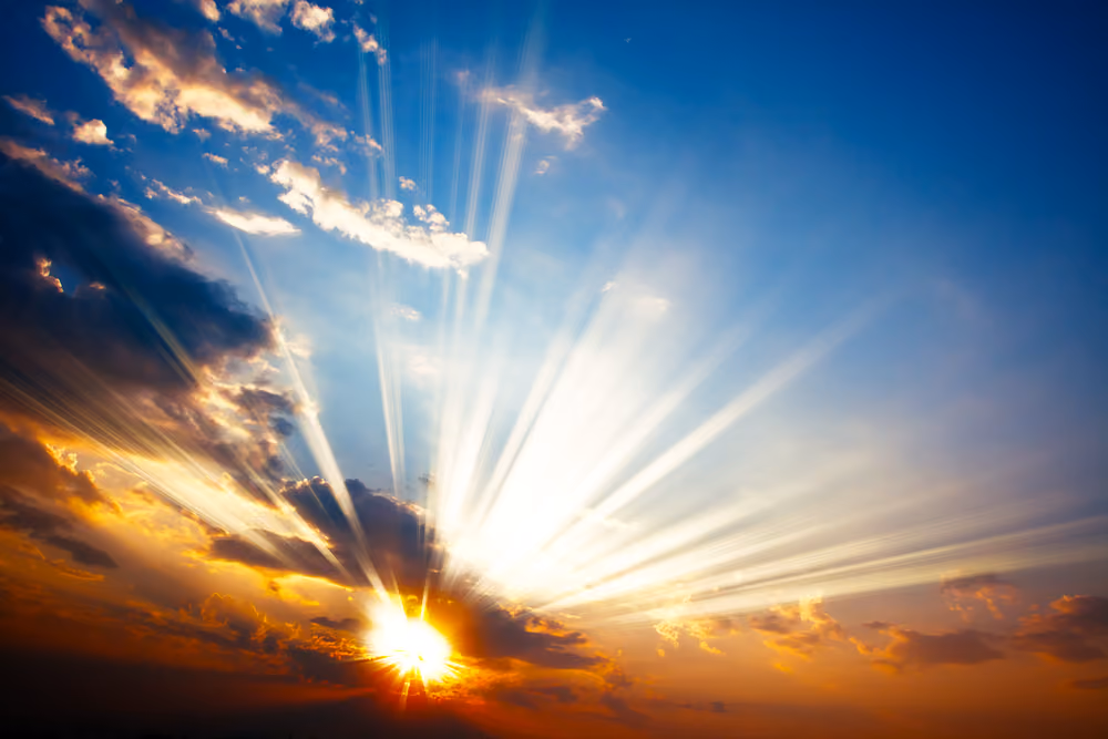 Sunset with sun rays streaming through scattered clouds in a colorful sky.