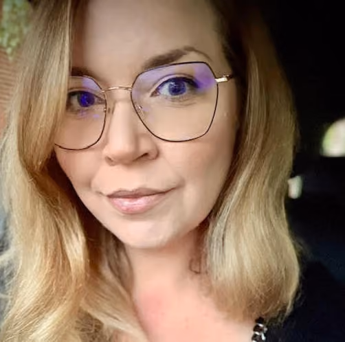 Close-up of a woman with blonde hair, wearing large glasses, looking into the camera.