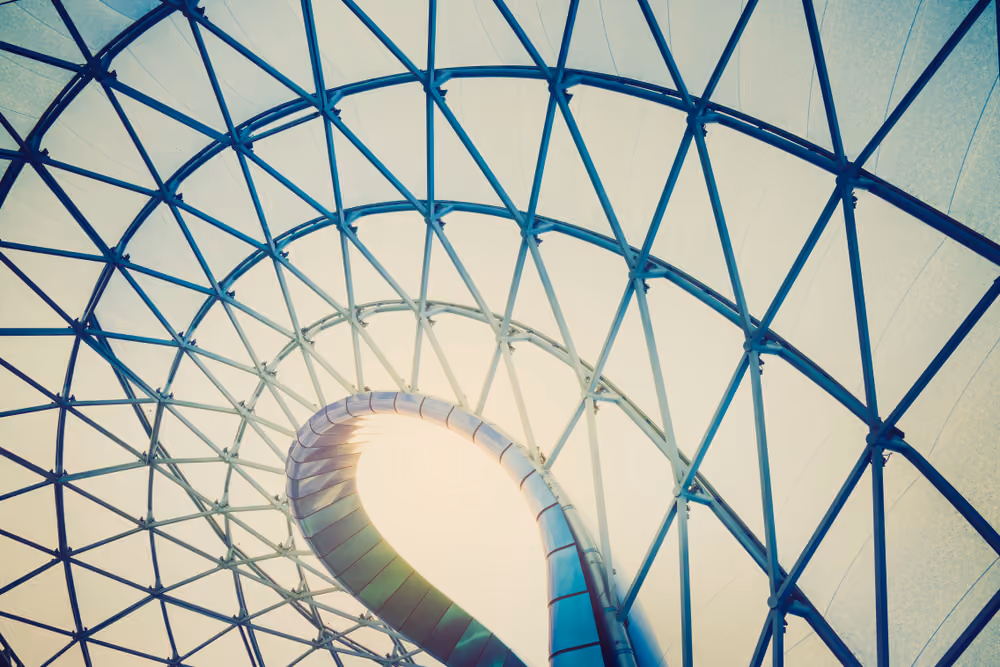 Curved metal staircase spirals upward inside a glass and steel lattice dome roof.
