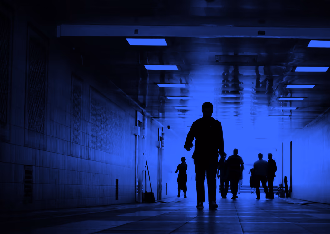 Silhouettes of people walking in a tiled underground passage with blue lighting.