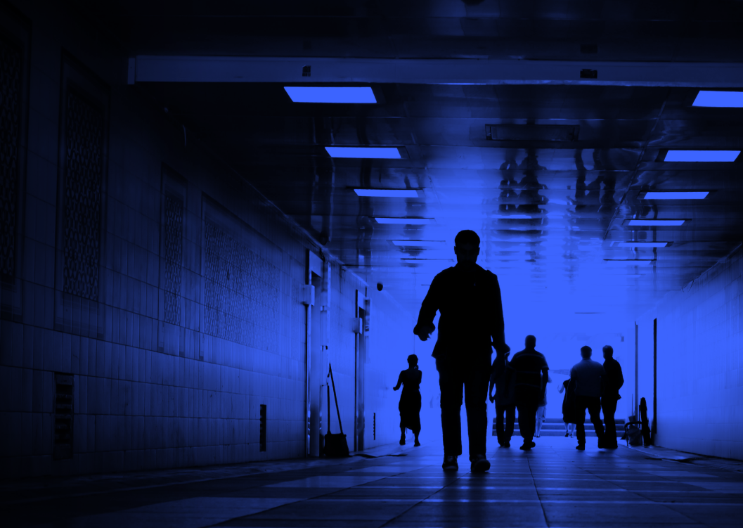 Silhouettes of people walking in a tiled underground passage with blue lighting.
