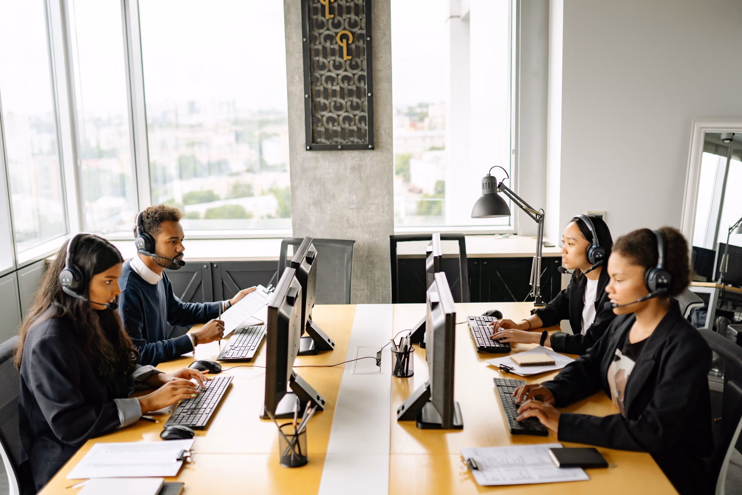 Four diverse call center agents wearing headsets working at computers in a modern office space.