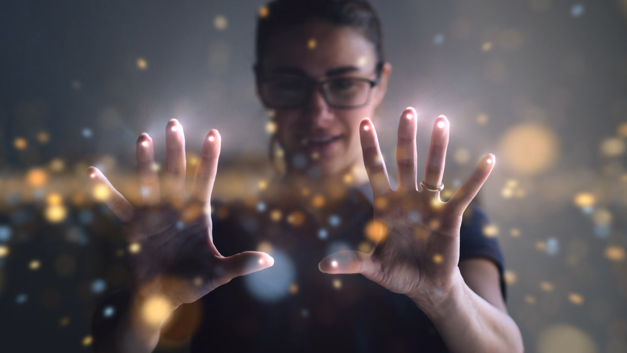 Person with glasses holding hands forward with glowing fingertips and sparkling light effects.